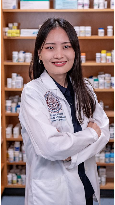 Smiling student in pharmacy lab wearing a white coat.