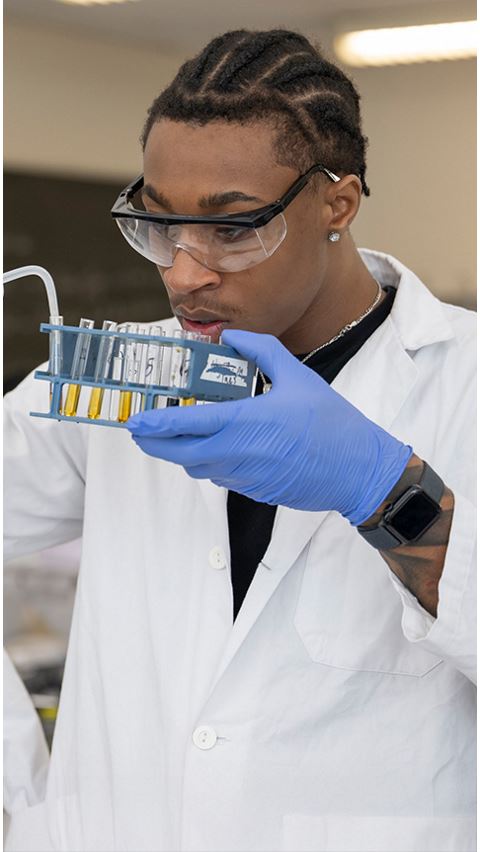Student in a white coat holding test tubes.
