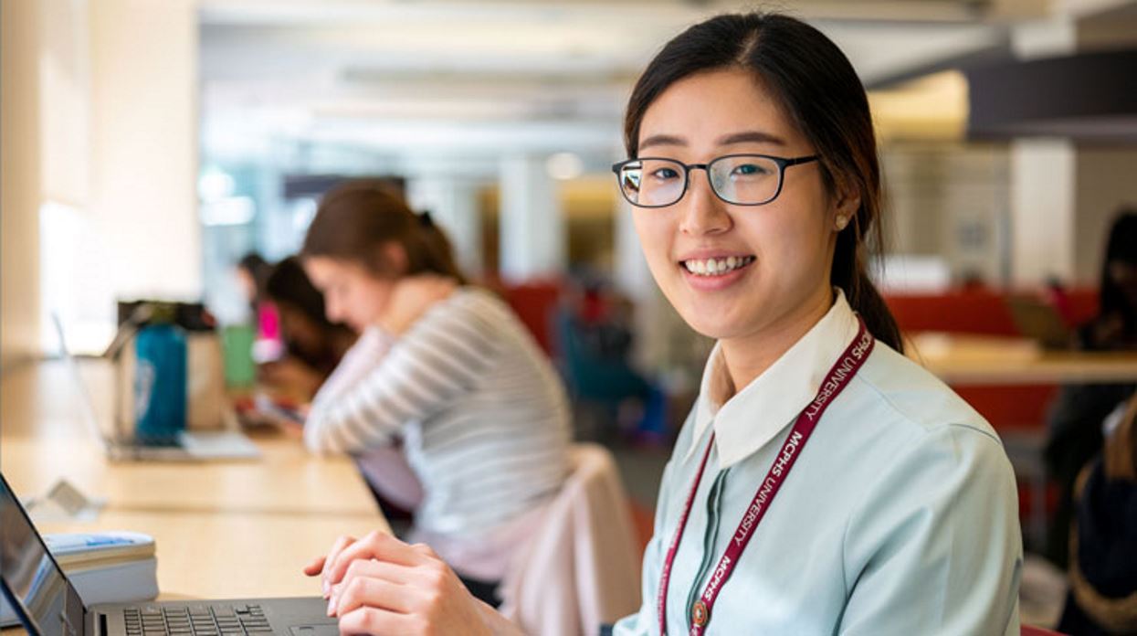 MCPHS student smiles for a picture while working on a laptop in the Henrietta DeBenedictis Library