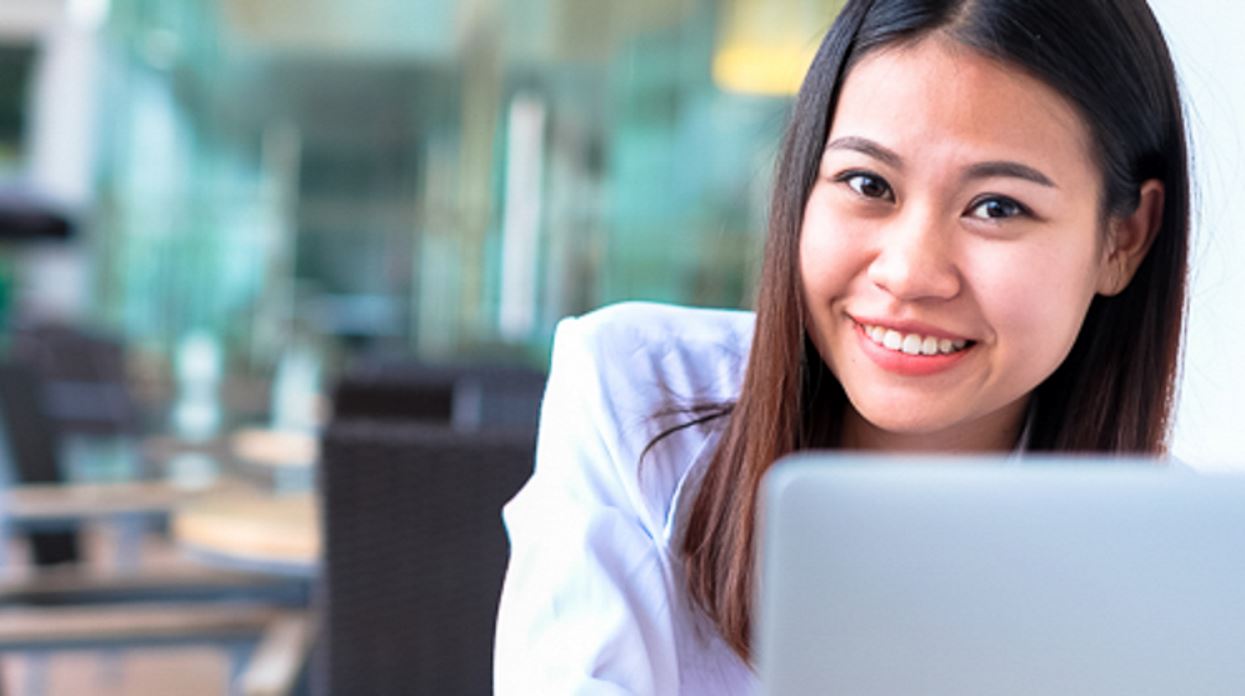 Close up photo of smiling MCPHS online student with laptop in classroom setting